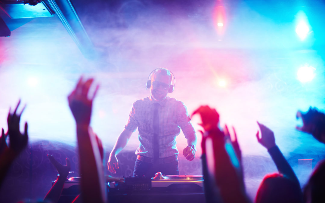 DJ standing by turntables in front of dancing crowd