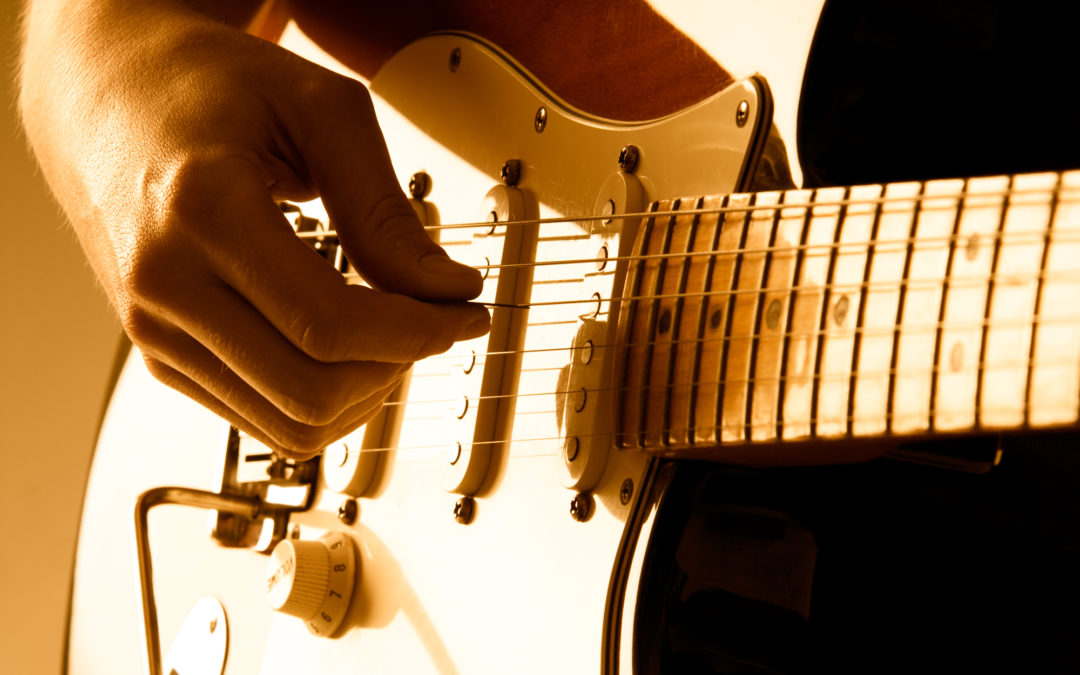 Hand picking guitar strings with shallow depth of field and orange lighting.